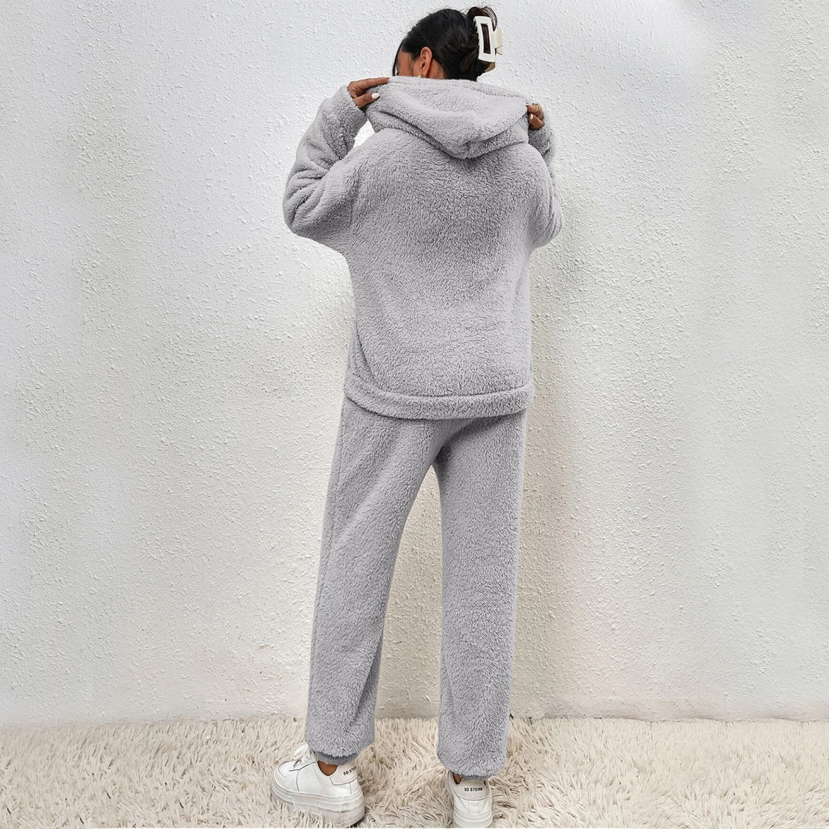 Person wearing a gray fleece tracksuit against a white wall.